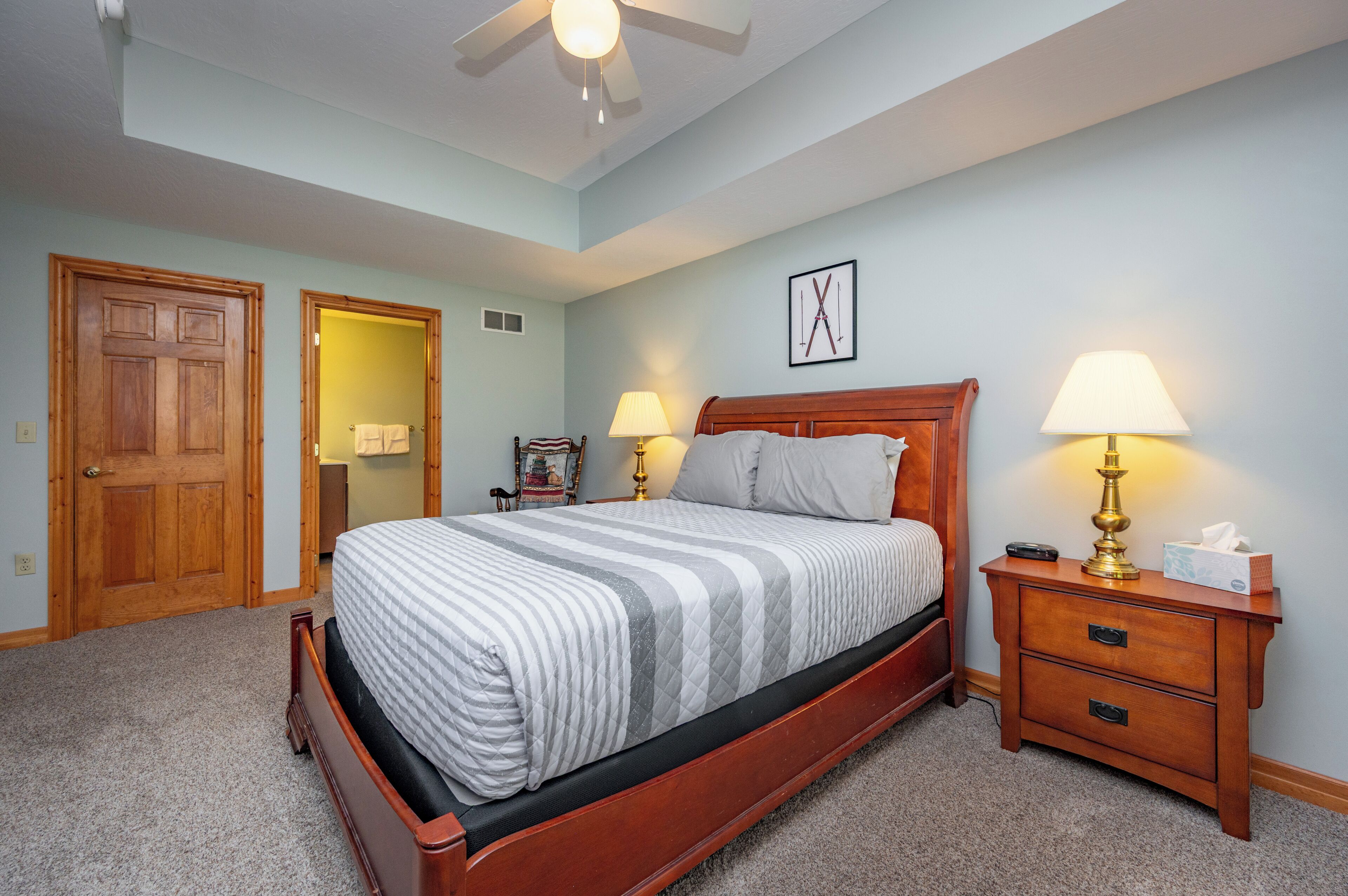 A bedroom with a wooden bed, two bedside lamps, a nightstand, and a door leading to another room.