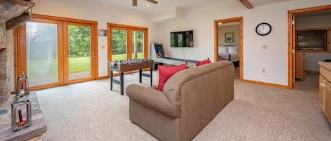 A spacious living room with a sofa, a foosball table, and a television.
