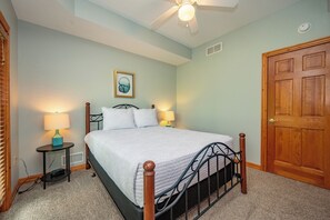Ein Schlafzimmer mit einem Bett, zwei Nachttischlampen, einem Deckenventilator, einer Tür und einem gerahmten Bild an der Wand.
