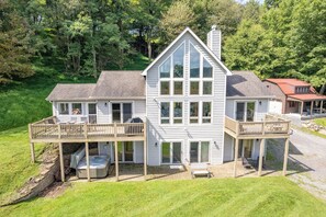 A large two-story house with a wrap-around porch, a hot tub, and a covered deck area. - New! Mountain Lake Area Getaway w/ Hot Tub! (Oakland)