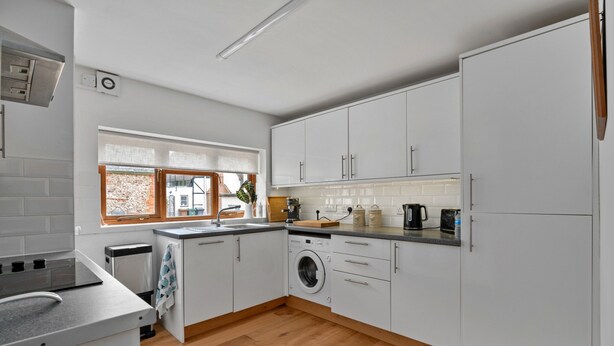 A modern kitchen with white cabinets, a built-in washing machine, and a window with a view of a brick building. - Romantic North Wales Meadow Cottage (Andover)