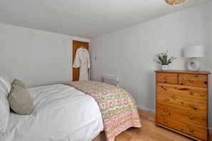 A bedroom with a bed, a dresser, a radiator, and a hanging robe. - Romantic North Wales Meadow Cottage (Andover)