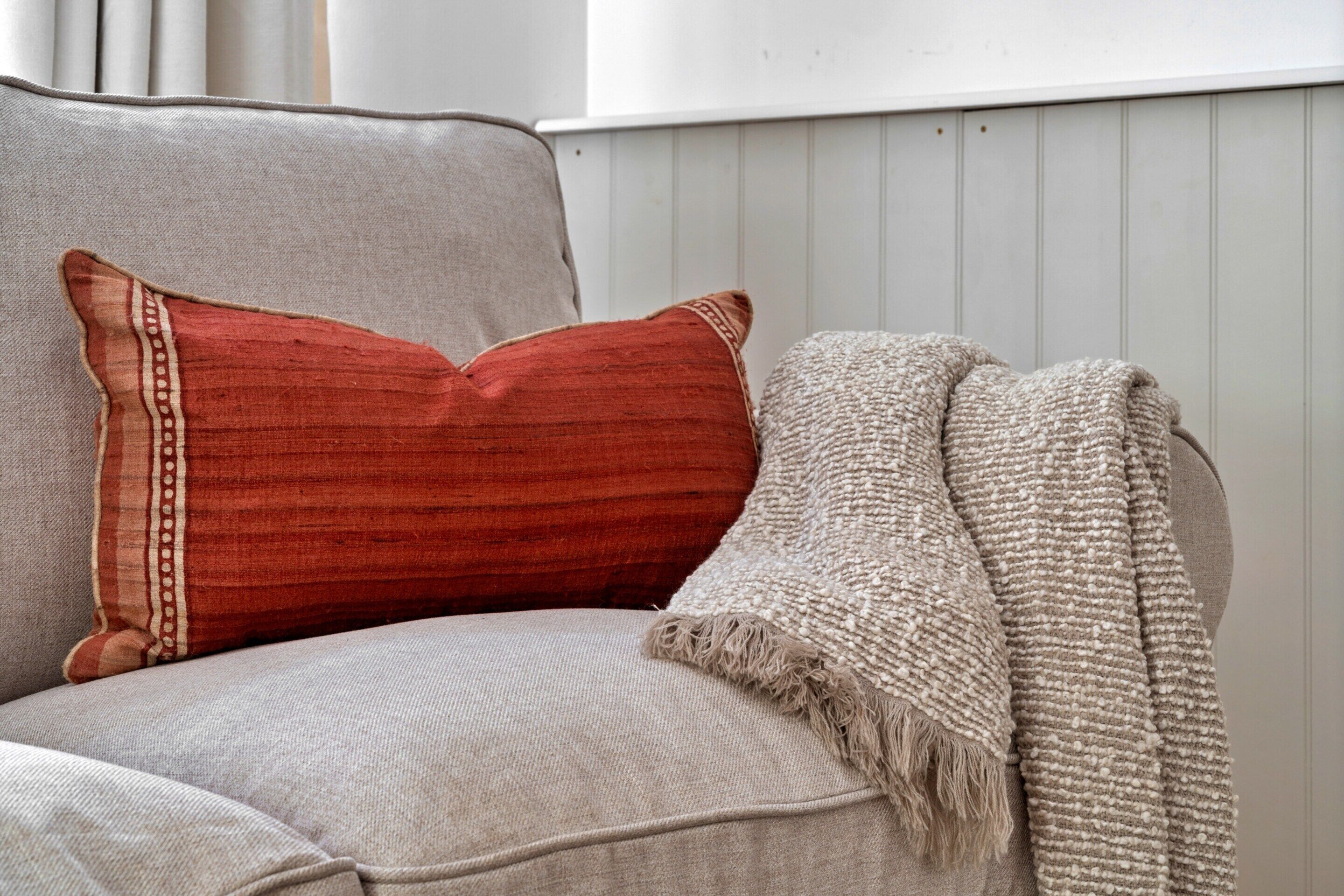 A sofa with a red pillow and a beige throw blanket.