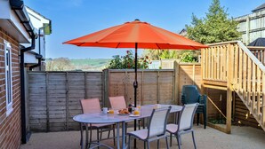 An outdoor patio with a table and chairs, a red umbrella, and a wooden fence. - Victorian Caernarfon House for 6 (Fowey)