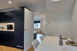Eine moderne Küche mit dunklen Schränken, einer Kaffeemaschine und einem Essbereich mit weißem Tisch und Stühlen.