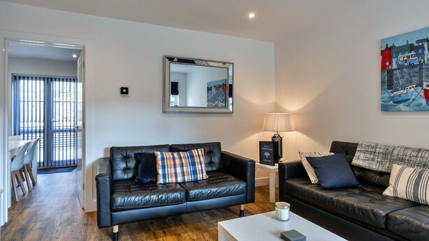 A modern living room with a black leather sofa, a white coffee table, and a painting on the wall. - Victorian Caernarfon House for 6 (Fowey)