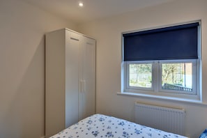 Ein Schlafzimmer mit Bett, Kleiderschrank, Fenster mit Blick und Heizkörper.