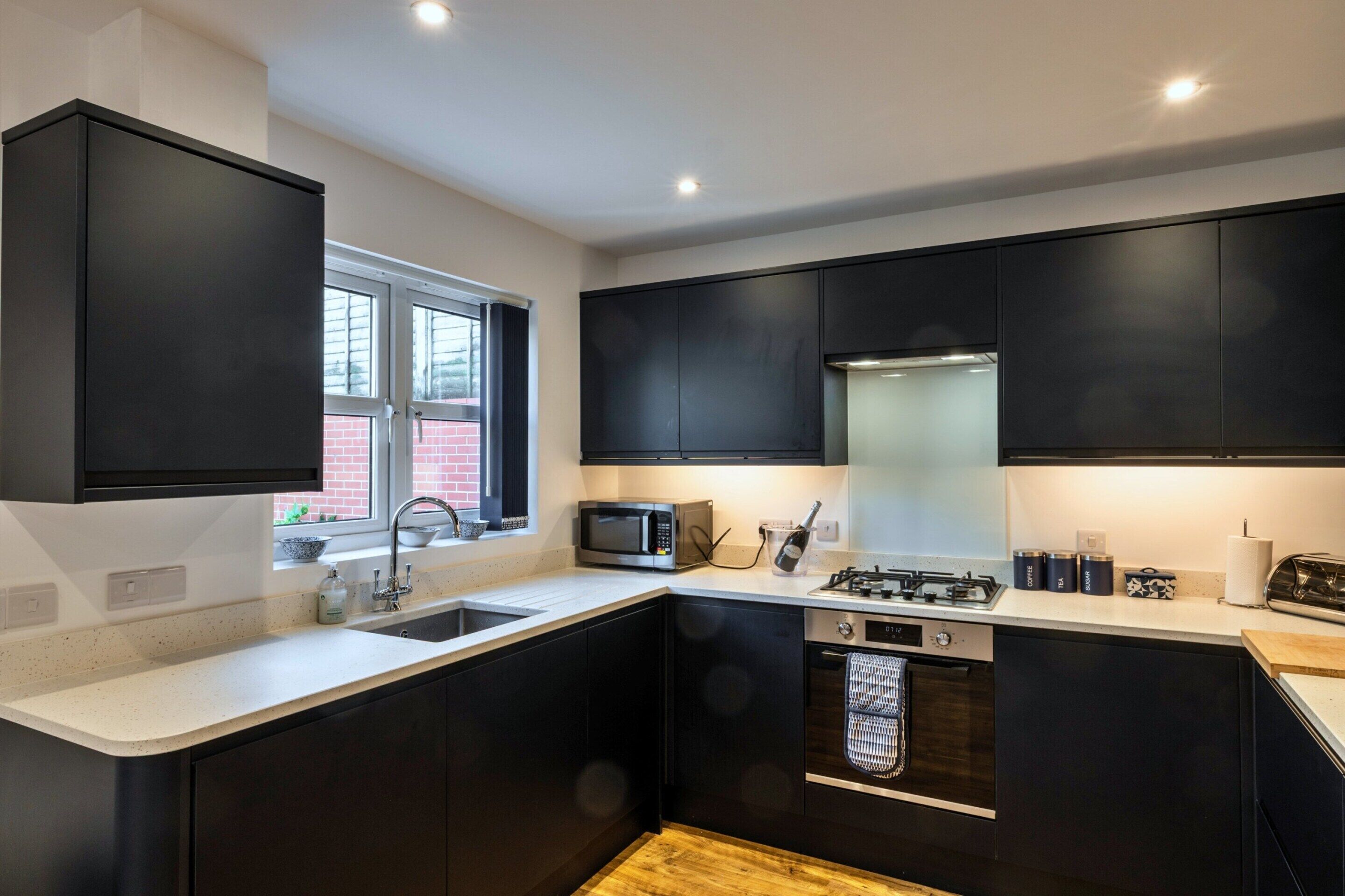 A modern kitchen with black cabinets, a stainless steel sink, a microwave, a gas stove, and a built-in oven.