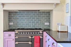 A kitchen with a gas stove, oven, and a tiled backsplash. - Pleasant Cottage in Banks of the River Fowey (Fowey)