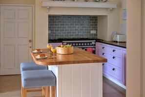 A kitchen with a wooden island, two blue barstools, a fruit bowl, and a toaster. - Pleasant Cottage in Banks of the River Fowey (Fowey)