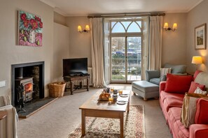 A cozy living room with a fireplace, a television, a sofa, and a dining table set for breakfast. - Pleasant Cottage in Banks of the River Fowey (Fowey)