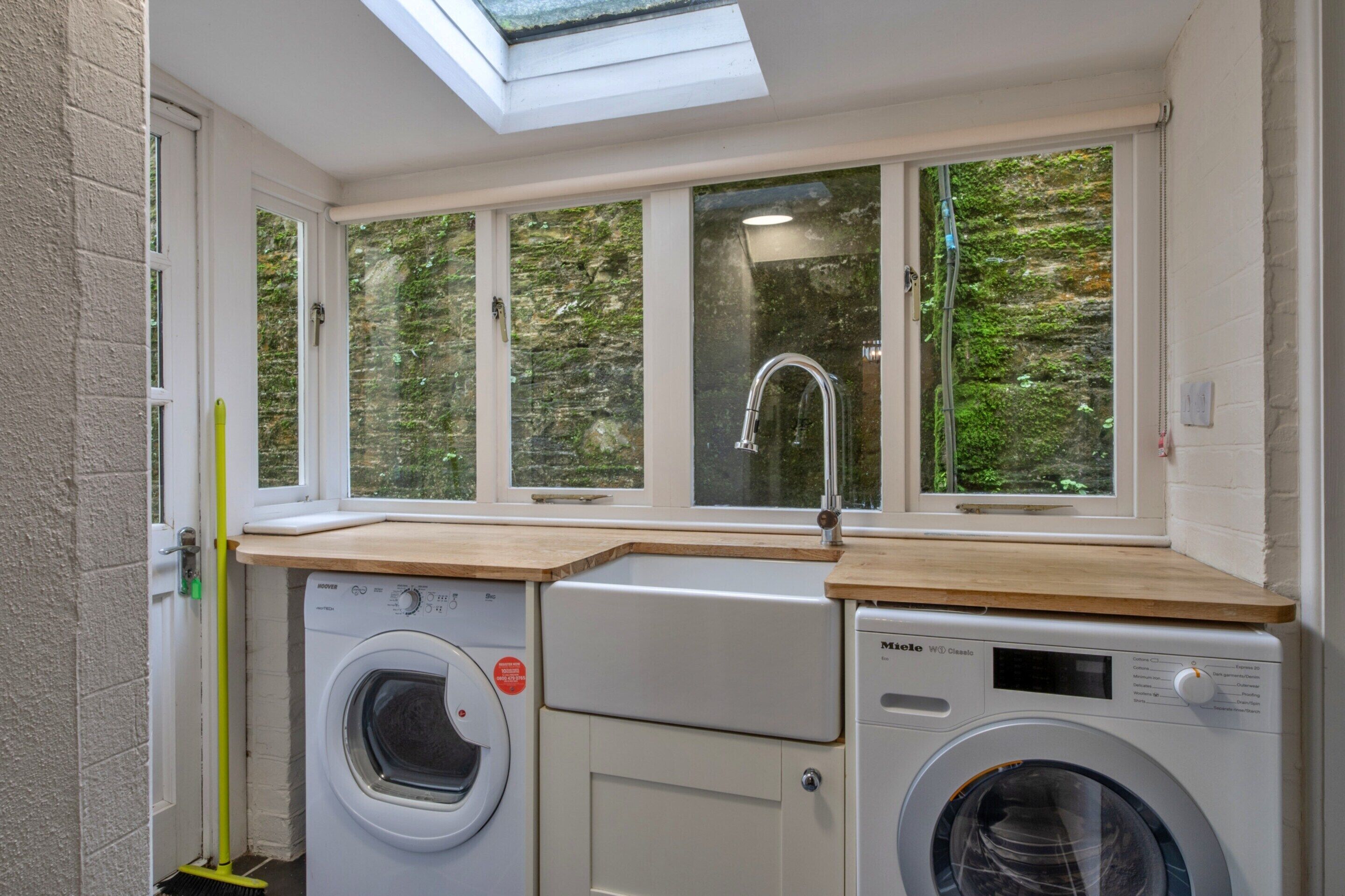 A laundry room with two washing machines, a sink, and a window with a view of greenery.