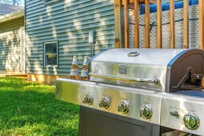 Ein Edelstahl-Grill mit vier Brennern, zwei Modelo-Bierflaschen und ein Holzzaun im Hintergrund.