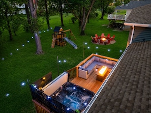 A backyard with a hot tub, a wooden play structure, and a seating area with outdoor furniture. - Hot Tub, Game Room with Arcades, 3 King Beds, Fire Pit - Sleeps 11 (St. Peters)