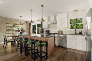 A modern kitchen with a central island, bar stools, stainless steel appliances, and a view of greenery outside. - Hot Tub, Game Room with Arcades, 3 King Beds, Fire Pit - Sleeps 11 (St. Peters)
