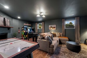 A living room with a pool table, a sofa, a gaming area with arcade machines, and a fireplace. - Hot Tub, Game Room with Arcades, 3 King Beds, Fire Pit - Sleeps 11 (St. Peters)