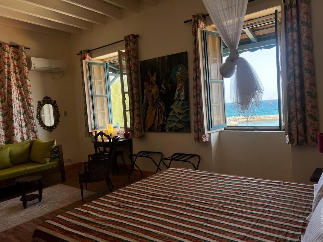 Une pièce comprenant un lit, un canapé vert, une table à manger avec des chaises, et une vue sur la plage par une fenêtre.