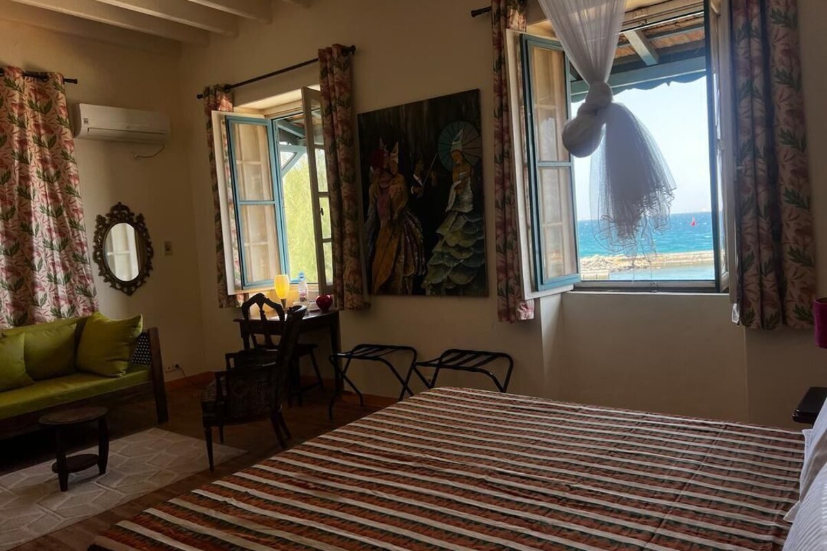 Una habitación con cama, un sofá verde, una mesa de comedor con sillas y vista a la playa por una ventana.