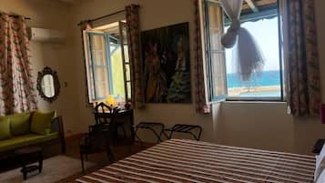 Une pièce comprenant un lit, un canapé vert, une table à manger avec des chaises, et une vue sur la plage par une fenêtre.