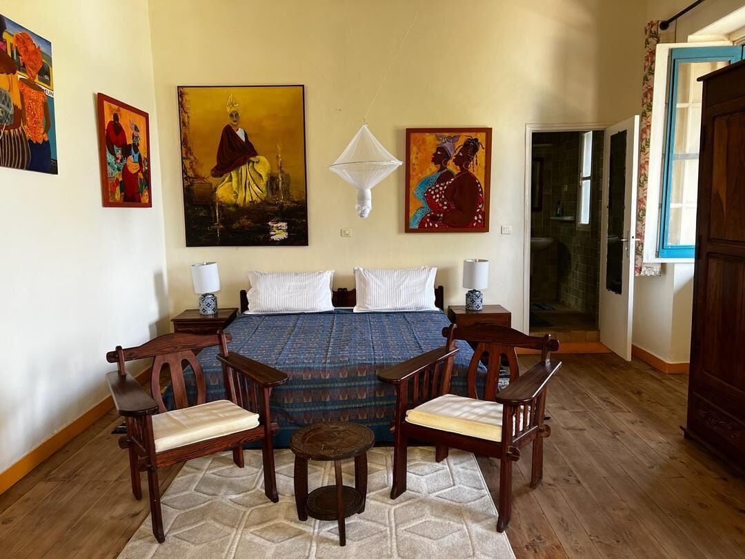 Een slaapkamer met een bed, twee nachtkastjes, een houten stoel, een klein tafeltje en kunstwerken aan de muur.