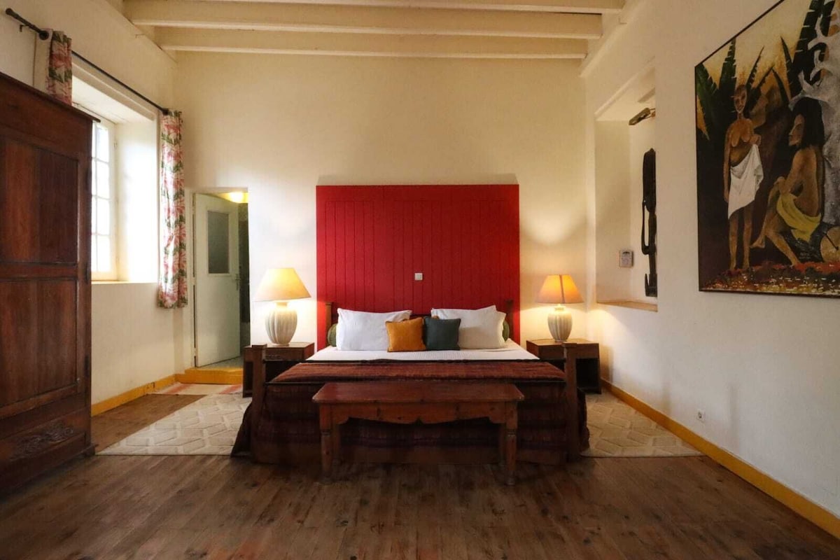 Un dormitorio con una cama de madera, dos lámparas de noche, un cabecero rojo y un cuadro en la pared.