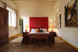 Un dormitorio con una cama de madera, dos lámparas de noche, un cabecero rojo y un cuadro en la pared.