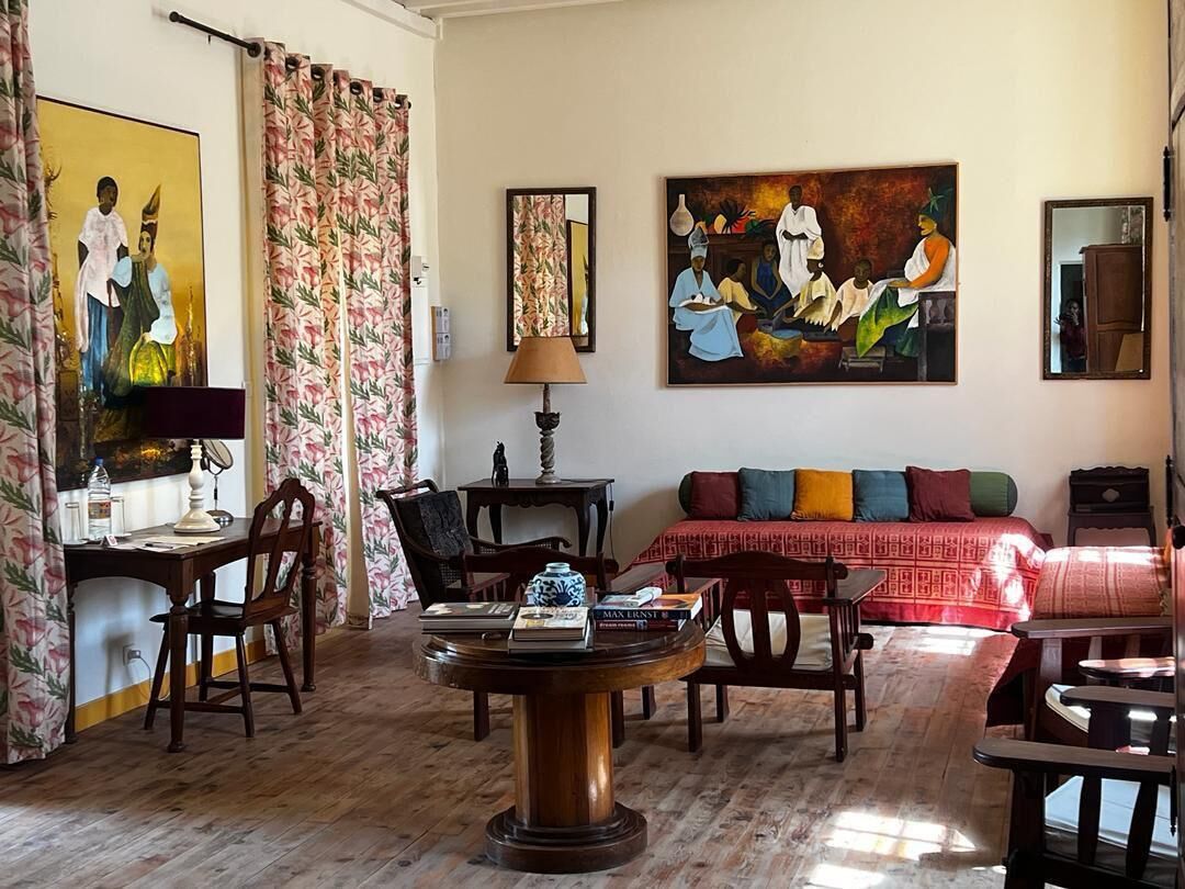 Une pièce avec un plancher en bois, une table ronde sur laquelle sont posés des livres, un canapé agrémenté de coussins colorés et deux tableaux accrochés au mur.