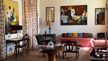 Une pièce avec un plancher en bois, une table ronde sur laquelle sont posés des livres, un canapé agrémenté de coussins colorés et deux tableaux accrochés au mur.