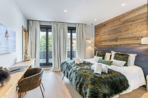 A modern bedroom with a large bed, a wooden headboard, a desk with a chair, and a view through a glass door. - Chalet-style apartment in Courchevel Village (Courchevel)
