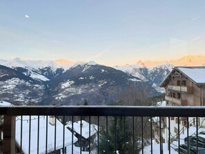 Blick auf Berge mit schneebedeckten Gipfeln und ein Holzhaus mit Balkonen.
