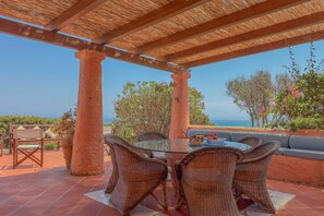 An outdoor patio with wicker furniture, a glass table, and a view of the sea. - Exclusive Villa Overlooking La Pelosa Beach (Stintino)