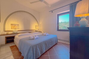 Een hotelkamer met een bed, twee bedlampen, een raam met uitzicht en een plafondventilator.