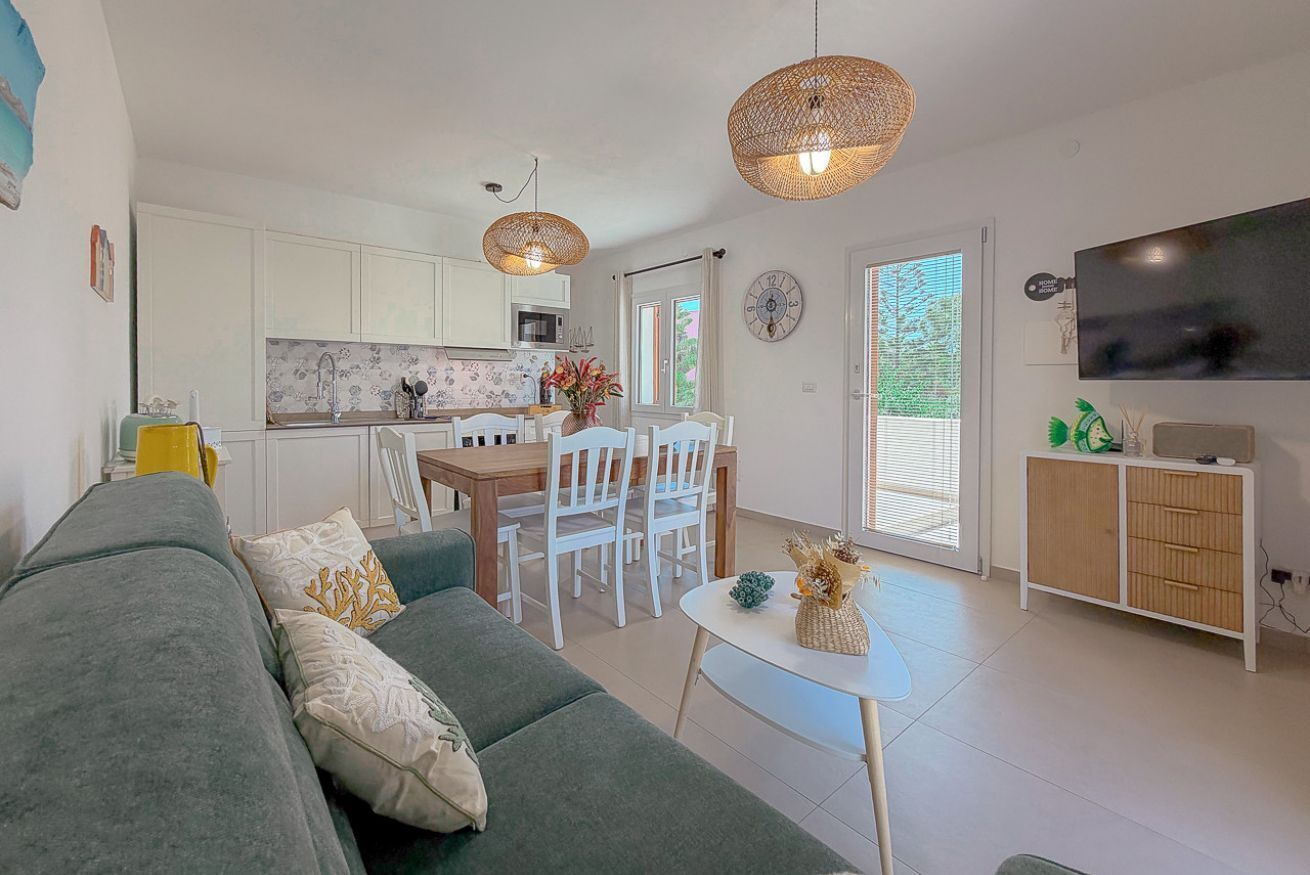 A modern living room with a sofa, a dining table with chairs, a kitchen area, and a television on a cabinet.