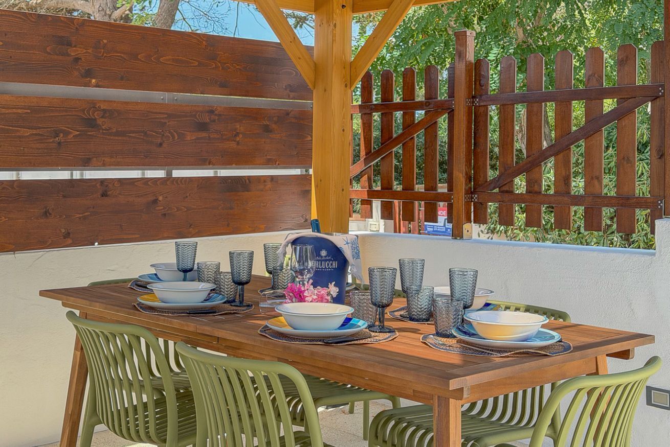 An outdoor dining area with a wooden table set for four, surrounded by green chairs.