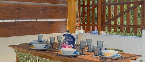 An outdoor dining area with a wooden table set for four, surrounded by green chairs.