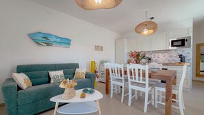 Ein Wohnzimmer mit einem grünen Sofa, weißen Stühlen, einem kleinen Tisch und einer Küchenzeile mit weißen Schränken und einer Mikrowelle.
