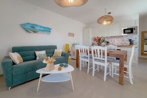 Ein Wohnzimmer mit einem grünen Sofa, weißen Stühlen, einem kleinen Tisch und einer Küchenzeile mit weißen Schränken und einer Mikrowelle.