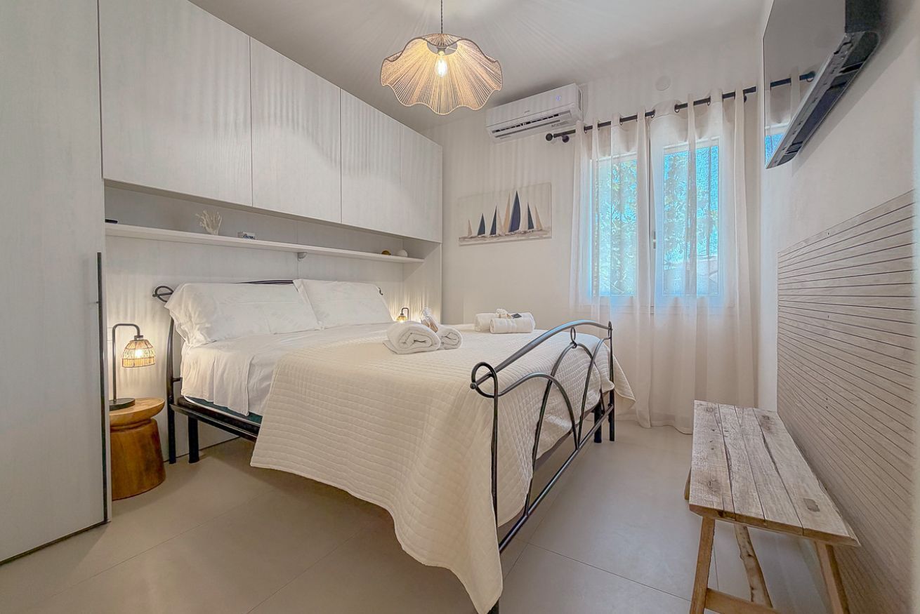 Ein Schlafzimmer mit einem Bett, Nachttischlampen, einer Holzbank und einem Fenster mit Vorhängen.