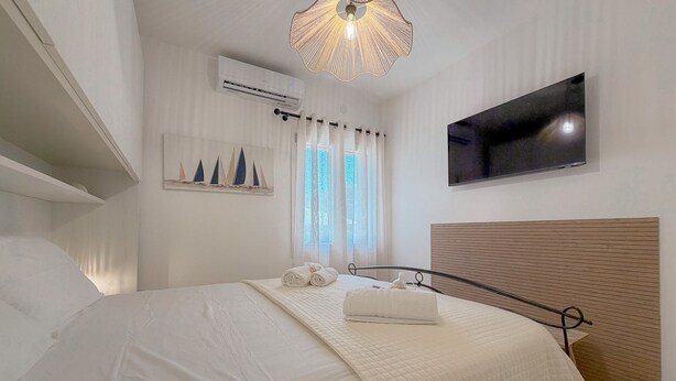 Ein Hotelzimmer mit einem Bett, einem Flachbildfernseher, einer Klimaanlage, einem Fenster mit Vorhängen und einem Wandbild von Segelbooten.