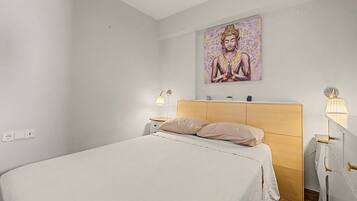 Een minimalistisch ingerichte slaapkamer met een bed, nachtlampjes, een houten hoofdbord en een schilderij aan de muur.
