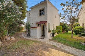 A two-story building with a stone pathway leading to the entrance, surrounded by greenery and potted plants. - Holiday Home 'Del Sol' with Shared Pool, Wi-Fi and Air Conditioning (Calafell)