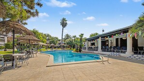 Piscina cercada por espreguiçadeiras e guarda-sóis, com um edifício ao fundo.