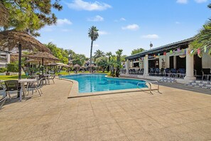 A swimming pool surrounded by lounge chairs and umbrellas, with a building in the background. - Holiday Home 'Del Sol' with Shared Pool, Wi-Fi and Air Conditioning (Calafell)