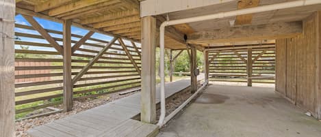 A covered outdoor area with wooden beams and a concrete floor, featuring a wooden deck and a metal railing.