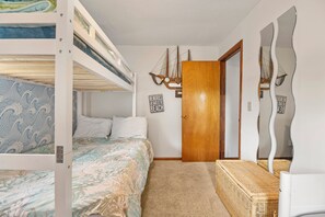 A bedroom with bunk beds, a wooden door, and a mirror with a wavy frame. - Eureka | Oceanfront with Great Views (Corolla)