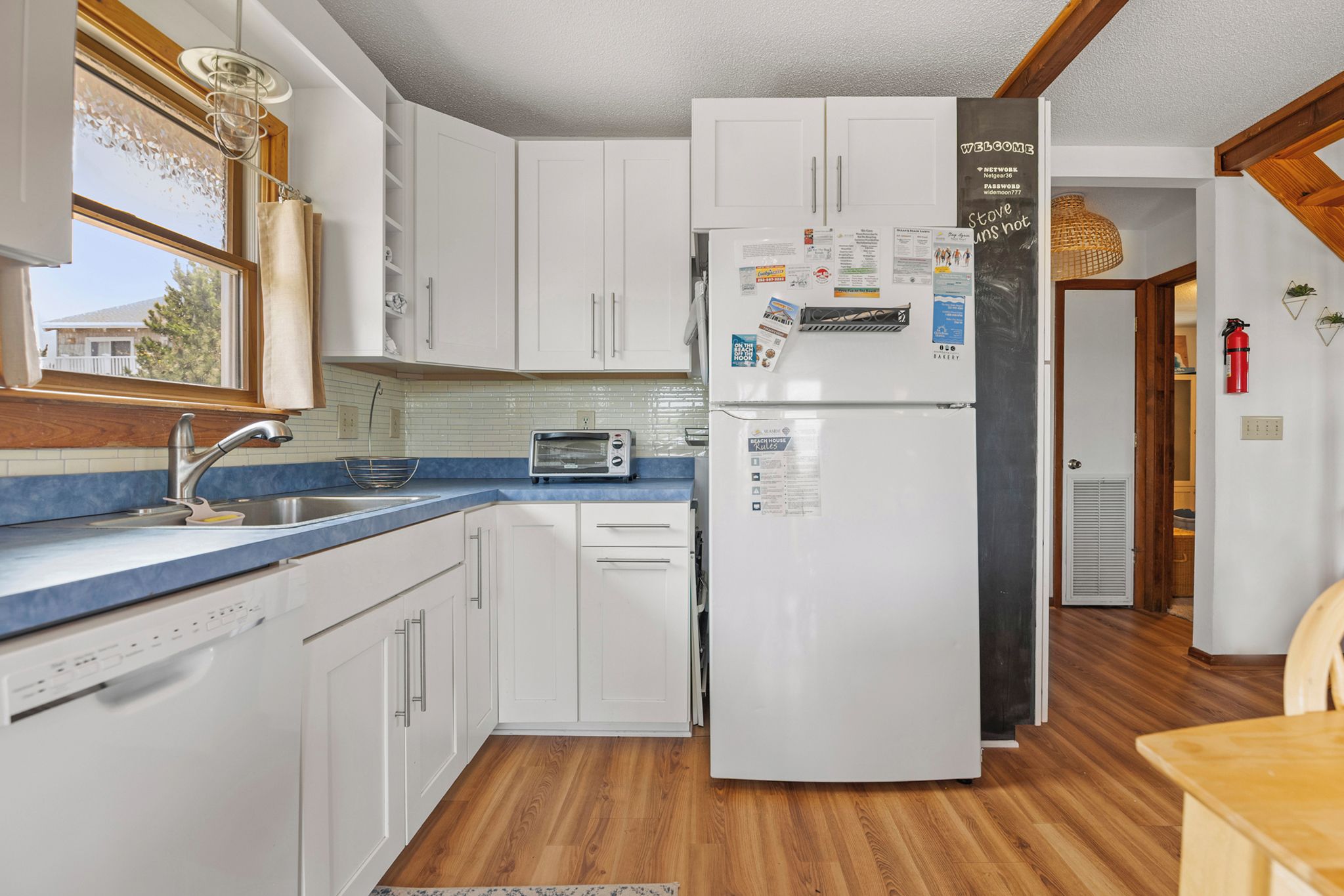 A kitchen with white cabinets, a built-in dishwasher, a toaster, and a refrigerator with magnets and papers.