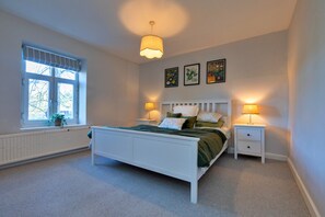 A bedroom with a white bed, two bedside tables with lamps, a window with blinds, and three framed botanical prints on the wall. - Cottage in Peak District National Park (Macclesfield)