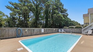 Piscina retangular com cerca de madeira e espreguiçadeiras.