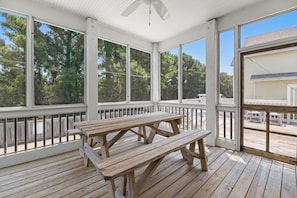 A covered outdoor area with a wooden picnic table and benches, surrounded by white railings and large windows. - Calm C's: Dog Friendly | Hot Tub | Pool (Corolla)
