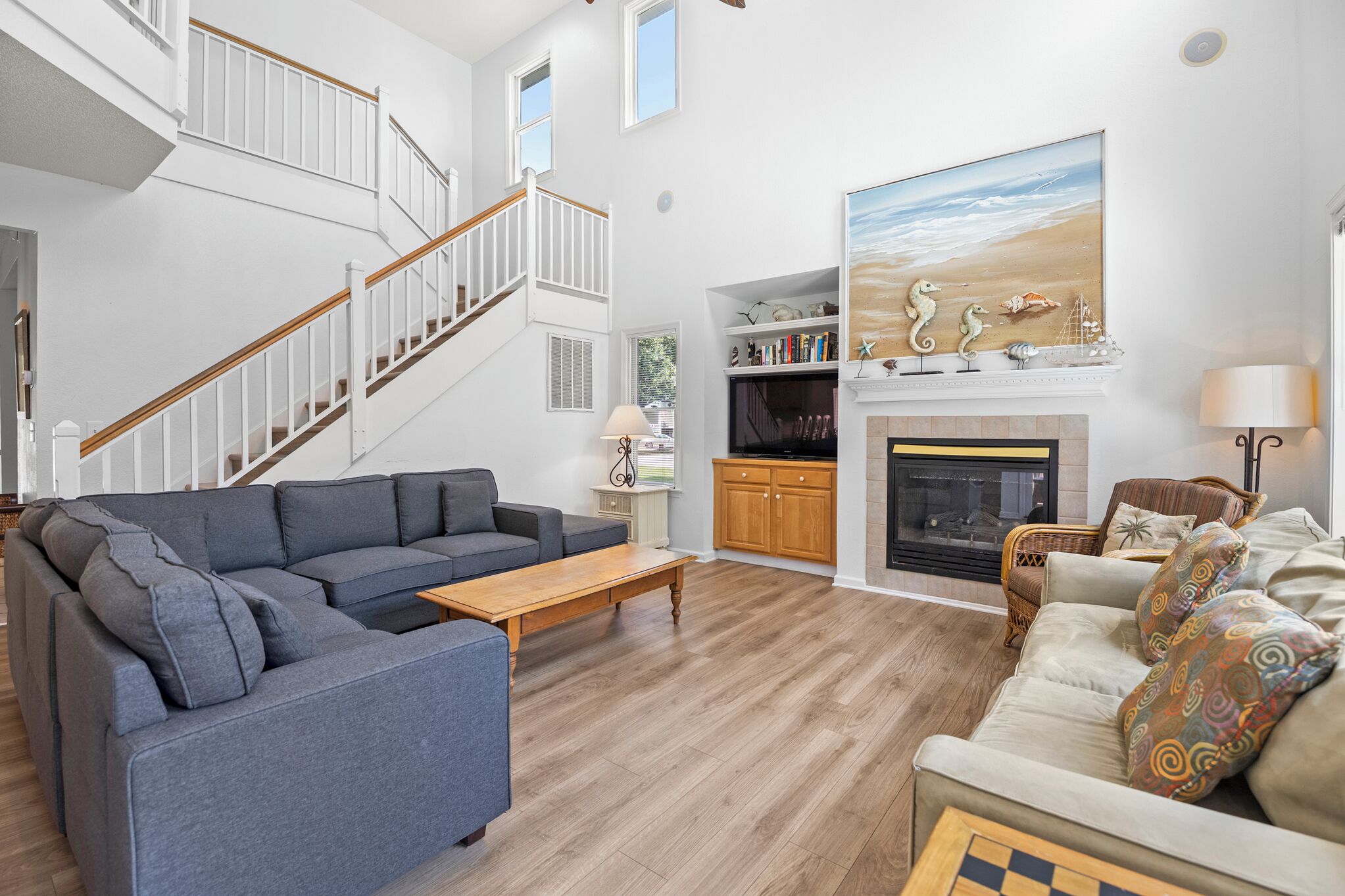 A spacious living room with a grey sectional sofa, a wooden coffee table, a fireplace, and a staircase.